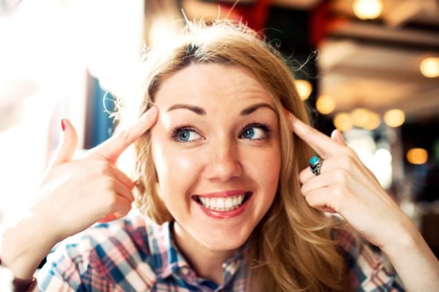 Imagem de uma mulher apontando seus dedos para a cabeça e sorrindo, como se estivesse pensando algo bom