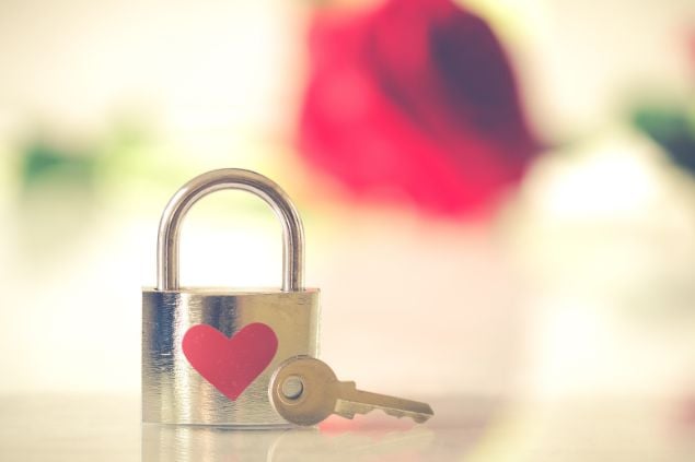 Imagem de um cadeado fechado com um adesivo de coração colado nele e uma chave ao lado prestes a abri-lo