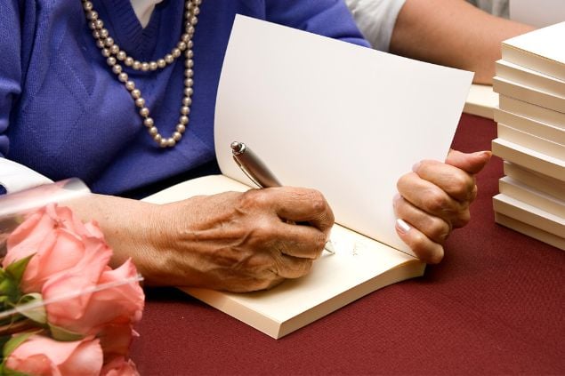 Imagem de uma senhora, dando um autógrafo em um livro