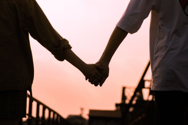 Imagem de um casal de mãos dadas e o céu alaranjado de fundo