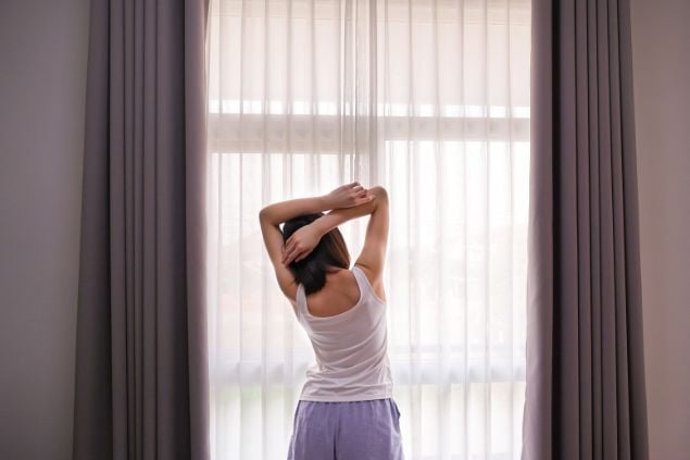 Imagem de uma mulher se espreguiçando na frente de uma janela grande com cortina