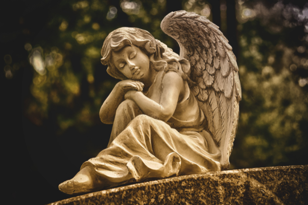 Estátua de um anjo sentado sob uma pedra com a cabeça apoiada em seus braços