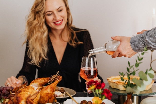 Mulher em uma mesa cheia de comidas natalinas esperando sua taça ser servida com vinho por um homem