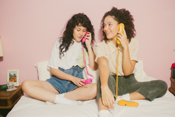 Duas mulheres sentadas na cama usando telefone de fio