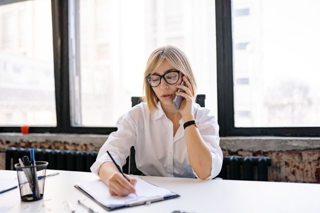 Mulher no trabalho falando no telefone e anotando em uma agenda