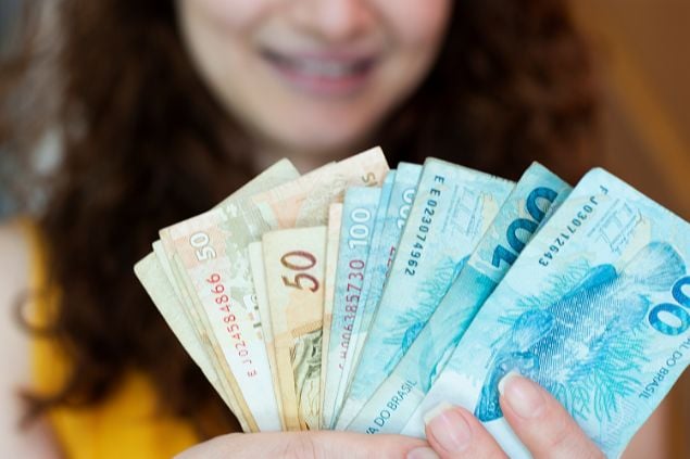 Imagem de uma mulher sorrindo e contando notas de 100 e 50 reais