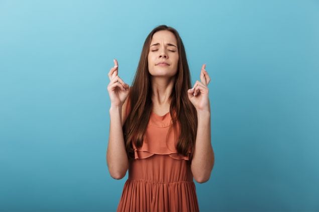Imagem de uma mulher fazendo figas com os dedos e com os olhos fechados