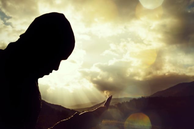 Imagem de um homem fazendo oração e atrás dele o céu ao entardecer