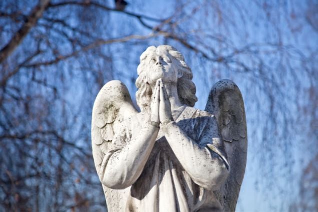 Imagem de uma estátua de um anjo orando com as mãos juntas