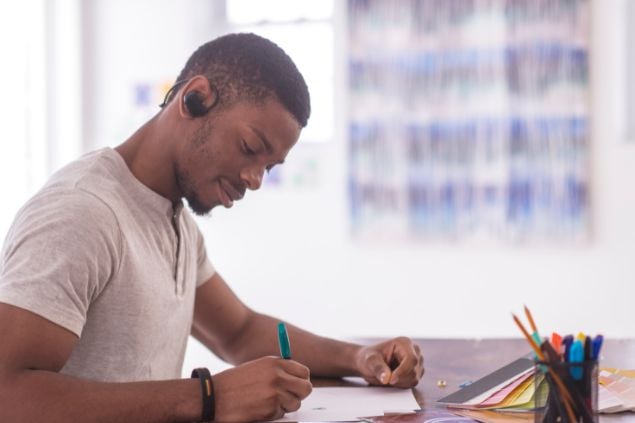 Imagem de um rapaz negro, com um fone de ouvido e estudando