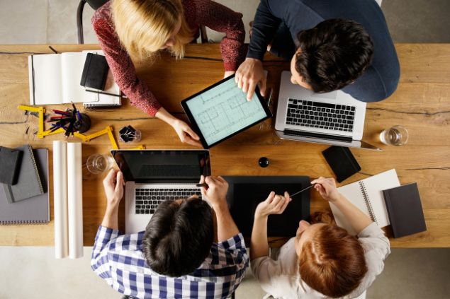 Quatro pessoas em uma mesa de escritório fazendo projetos no tablet