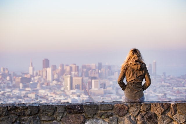 Mulher loira sentada de costas observando a cidade.